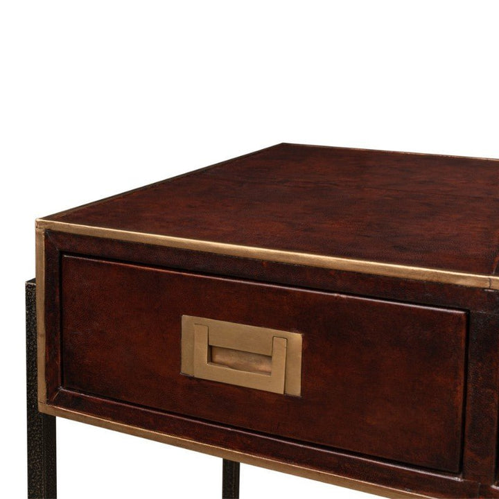 A close-up view of a dark brown wooden nightstand with a single drawer. The drawer features a brass handle with an inset rectangular design. This Sarreid Old Leather Desk-inspired nightstand has a sturdy, minimalist iron frame and exudes transitional style.