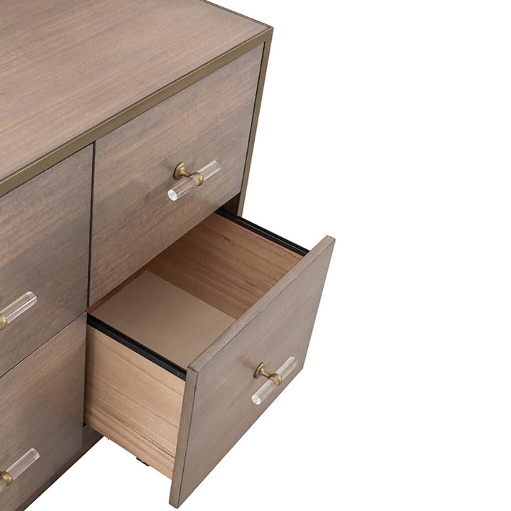 A wooden dresser crafted from eucalyptus wood with a Grecian Clay finish features six drawers, two of which have clear, vertical acrylic handles with gold accents. The bottom right drawer is partially open, revealing an empty interior. The dresser surface has a smooth finish reminiscent of the Park Avenue Lateral File Cabinet by Fairfield Chair.