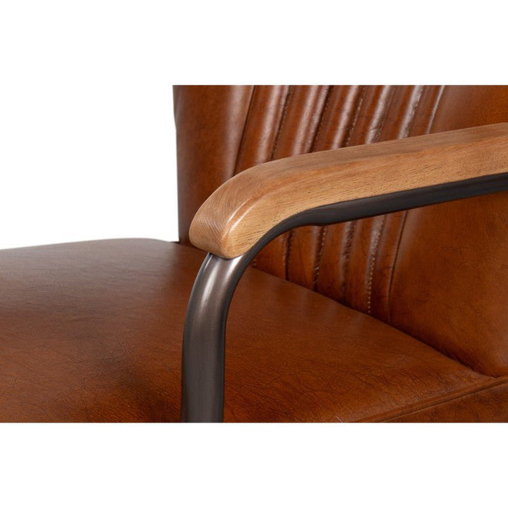 Close-up of the Parker Office Chair's armrest, showcasing a blend of materials: a sleek, light brown wooden top rail attached to a black metal armrest. The cushioned seat and backrest of the chair from Sarreid are upholstered in rich, top-grain Vintage Havana leather with visible stitching details.