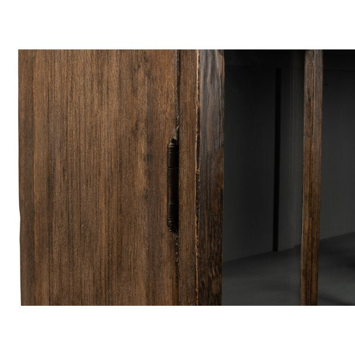 Close-up of a wooden cabinet door showcasing a dark stained finish, part of the Refined Arches Tall Bookcase by Sarreid. The image highlights the metal hinge and a portion of the glass panels on the right side. The wood grain is visibly textured, enhancing the rustic appearance of this refined piece.