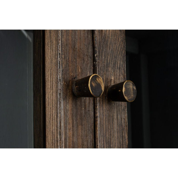 Close-up of two dark wooden cabinet doors with aged brass knobs, showcasing the rustic texture of the weathered wood and the worn appearance of the metal hardware. The background is dark, emphasizing the vintage look of this traditional style Refined Arches Tall Bookcase by Sarreid.