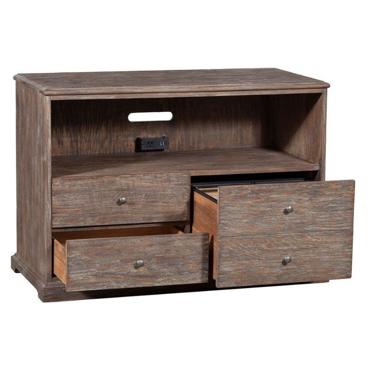 The Rustique Lateral File Cabinet by Fairfield Chair exudes rustic elegance with its wooden construction and rustic finish. It features an open shelf equipped with a cable management hole and two electrical outlets for modern functionality. Below the open shelf are three drawers, reminiscent of those in the Rustique Lateral File Cabinet, all partially open to showcase storage space.