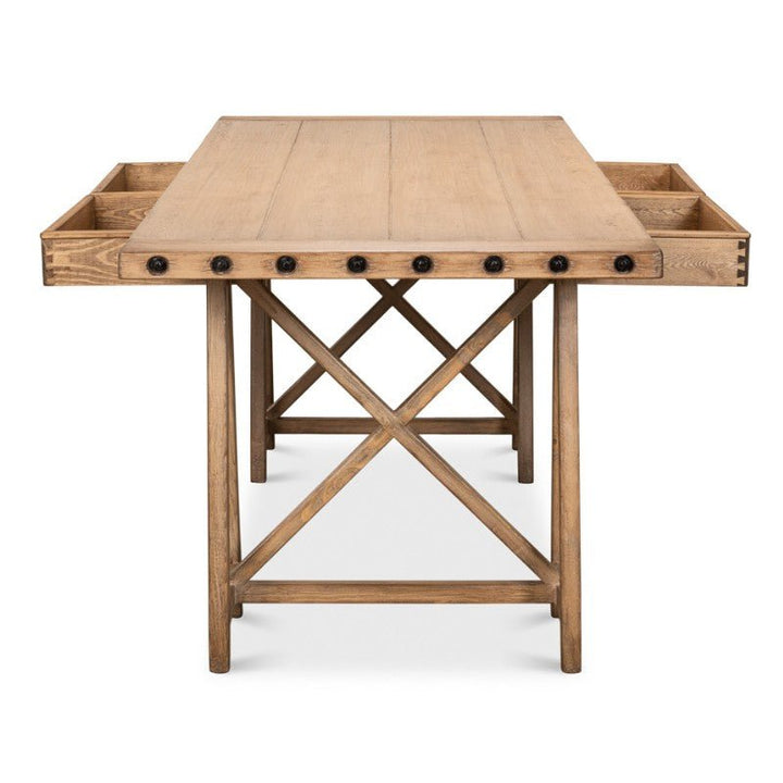 The Sarreid Sawhorse Desk, Natural Polished Old Pine 87", is a wooden table crafted from reclaimed pine with a rectangular top, featuring built-in storage compartments on both sides. The desk has an X-shaped support structure underneath and visible black knobs along the edge, adding to its rustic charm. The wood boasts a light, natural finish.