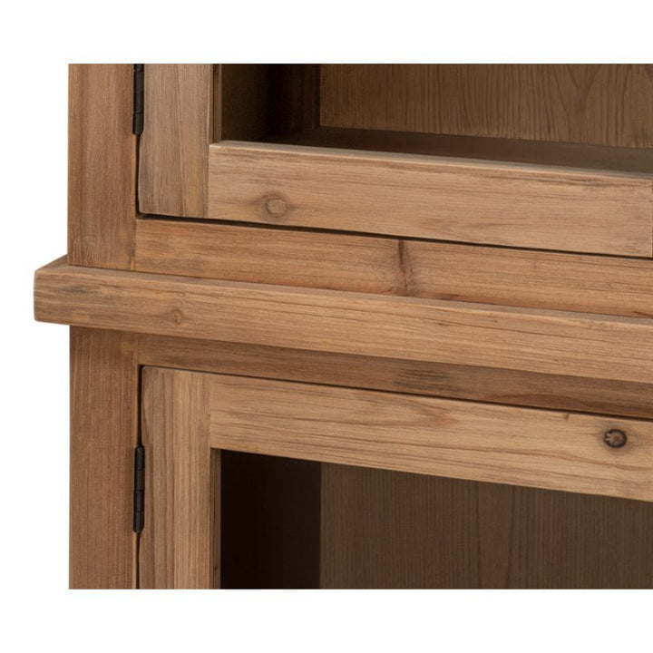 A close-up of a section of the Tanner Bookcase, Natural by Sarreid, crafted from reclaimed pine. The image showcases the corner where two parts meet, emphasizing the wood's grain and texture, which is enhanced by a natural brushed finish. The wood appears to be unfinished or lightly stained, with hinges attaching the doors.