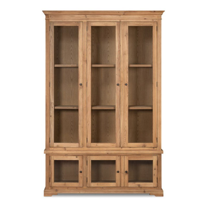 The Tanner Bookcase by Sarreid is a tall, wooden display cabinet with a natural brushed finish. It features three glass-paneled doors on the top section, each containing two shelves inside, and two smaller glass-paneled doors at the bottom with a single shelf inside each. The bookcase is constructed from reclaimed pine and is accented with black knobs.