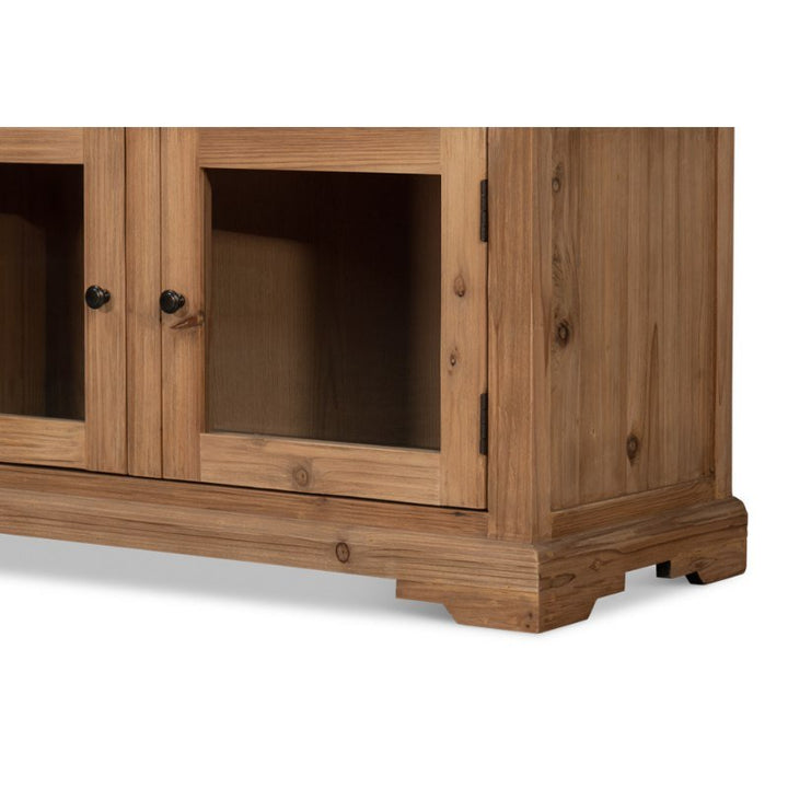 The Tanner Bookcase, Natural by Sarreid features a wooden cabinet with a natural brushed finish, glass-paneled doors, and black knob handles. Crafted from reclaimed pine, the construction showcases prominent wood grain for a rustic appeal. The base includes simple decorative molding, and the hinges are visible on the right side.