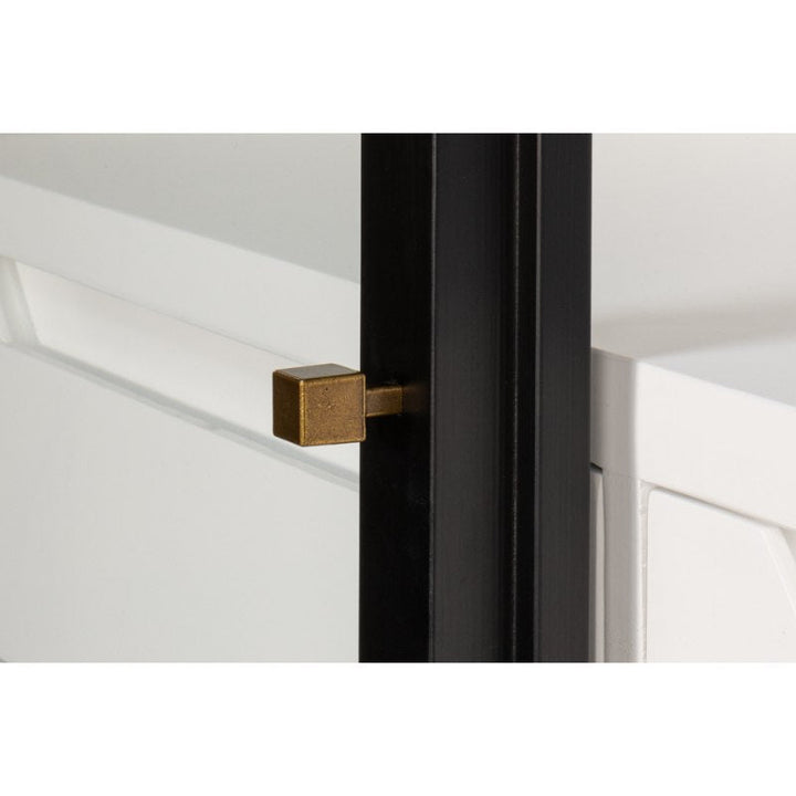 A close-up of a sliding door with a modern design, featuring a brushed black exterior frame and a gold square doorstop. The door appears to be part of a sleek interior fixture with clean lines and a minimalist style, complementing the Walker Bookcase in black by Sarreid in the background.